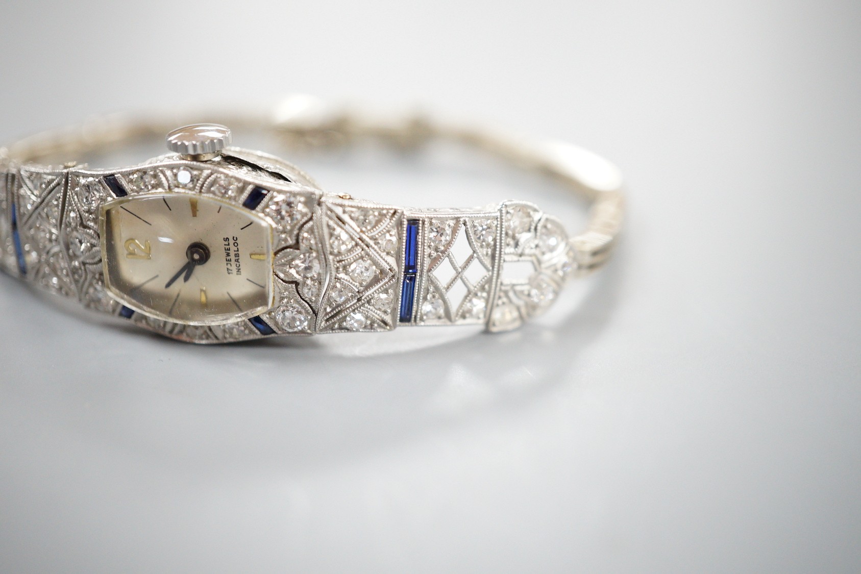 A lady's mid 20th century white metal, sapphire and diamond cluster set cocktail watch, on a 9ct bracelet (a.f.), gross weight 17.2 grams.